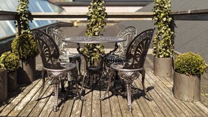 A wooden deck with a round table and four chairs, surrounded by potted plants and climbing vines.