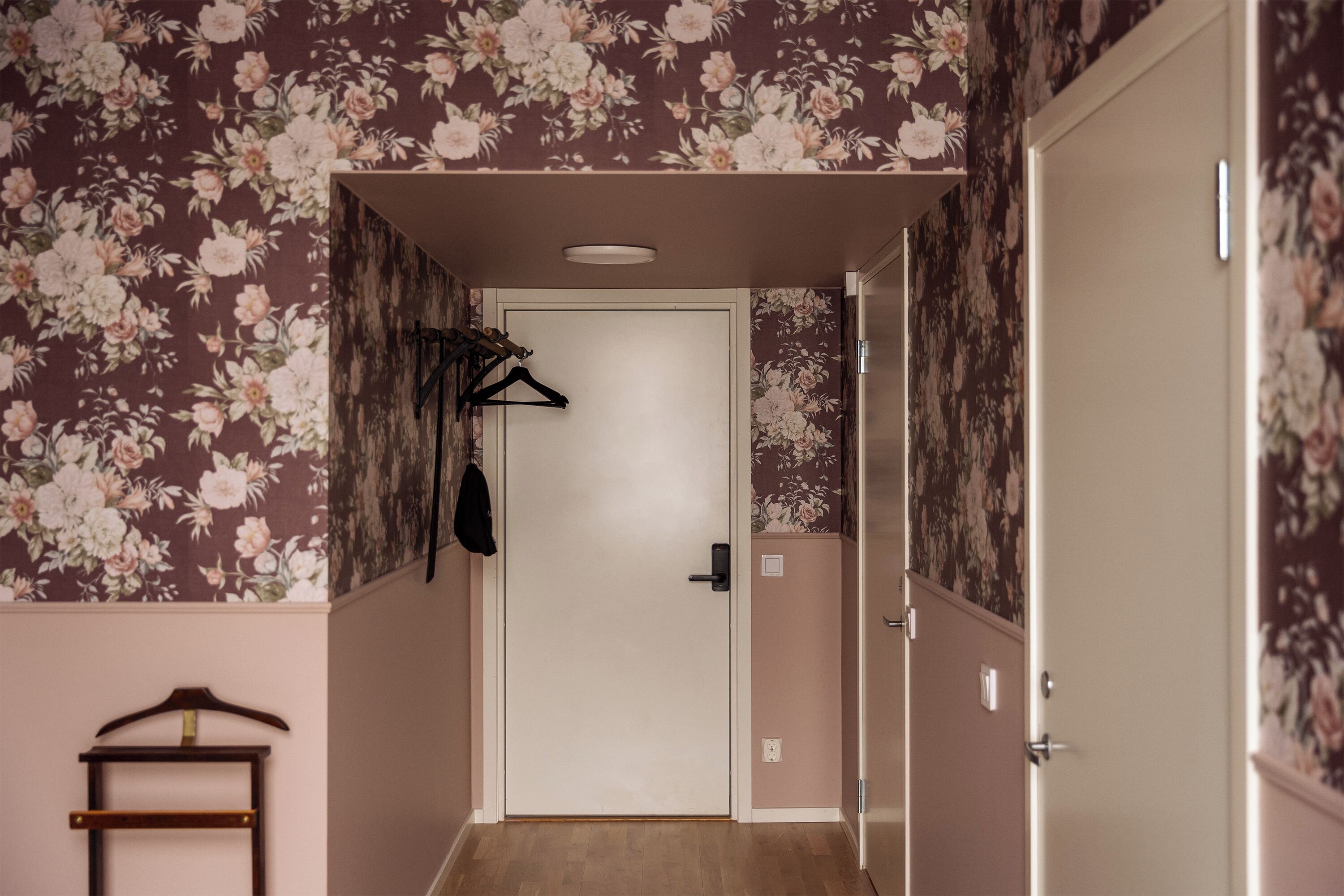 A hallway with floral wallpaper, a coat rack, and a door leading to another room.
