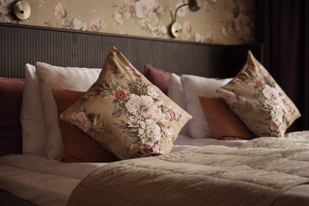 Un lit avec des oreillers à motifs floraux et une couverture beige à texture.