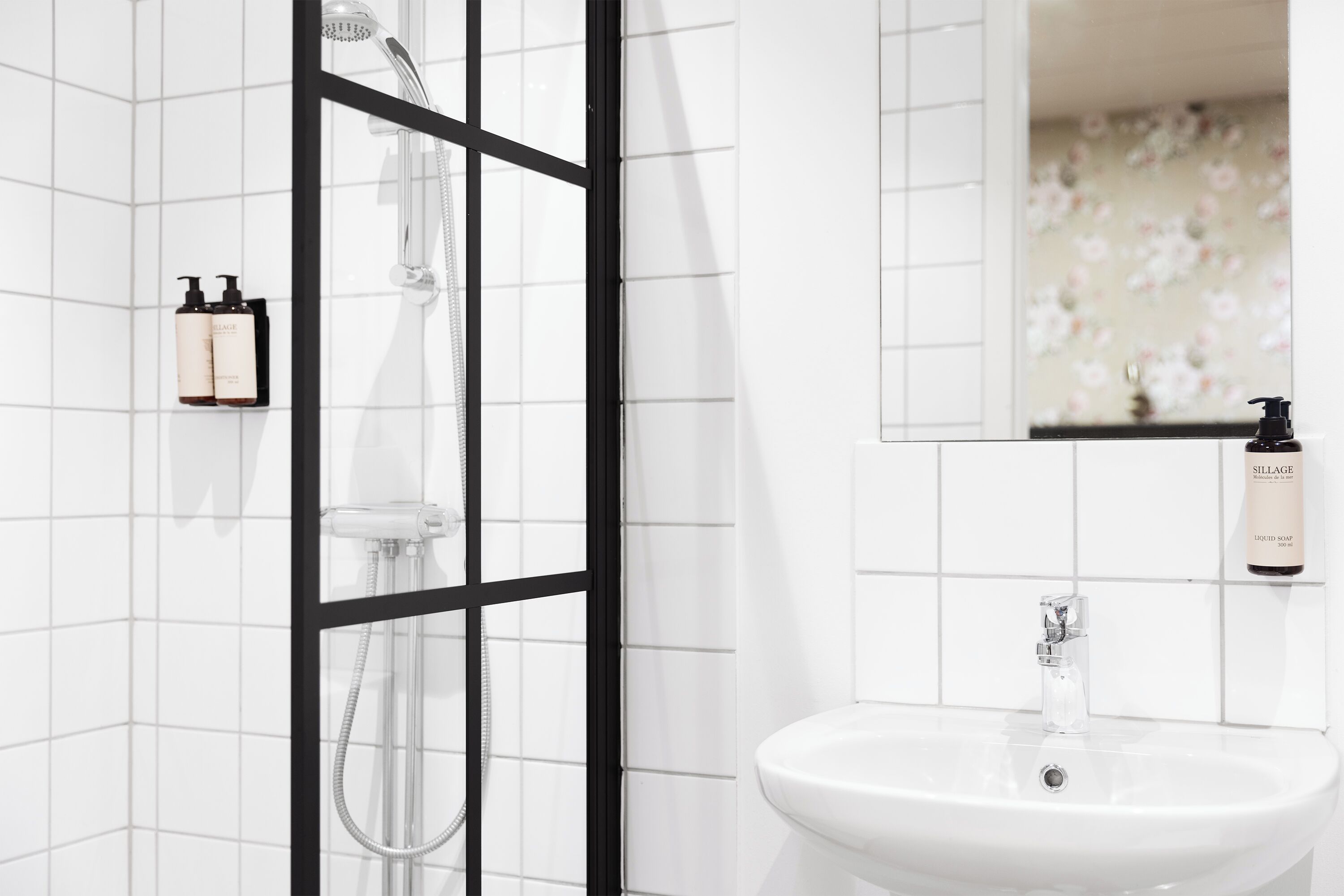 Un baño moderno con ducha, lavabo y botellas de artículos de tocador en la pared.