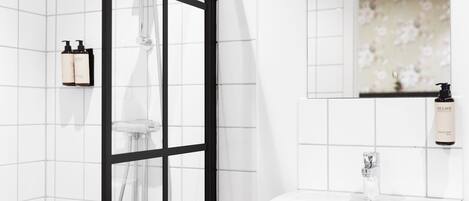 Un baño moderno con ducha, lavabo y botellas de artículos de tocador en la pared.