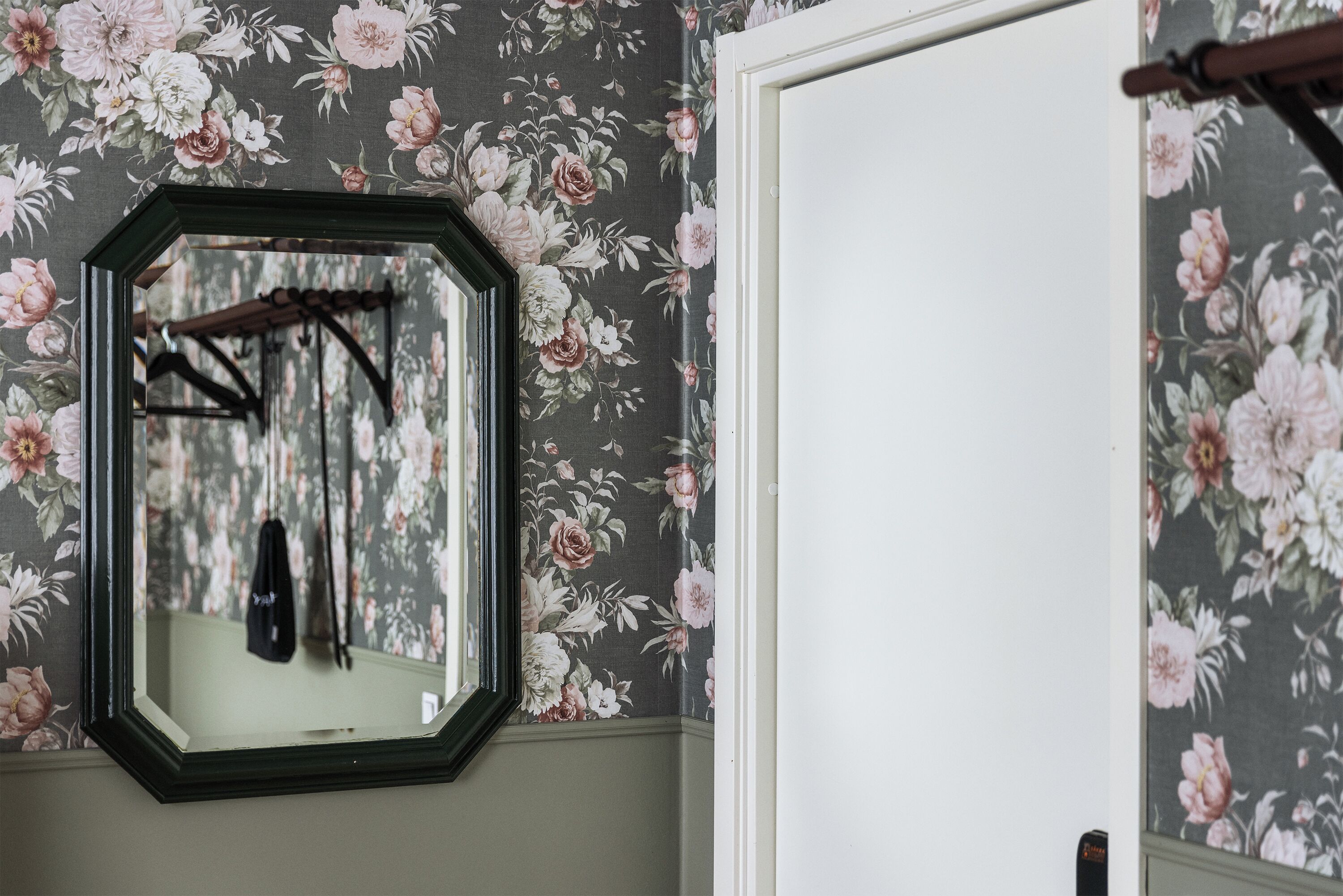Um quarto com papel de parede floral, um espelho e uma porta.