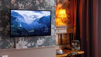 A television mounted on a floral wallpaper wall displaying a mountainous landscape.