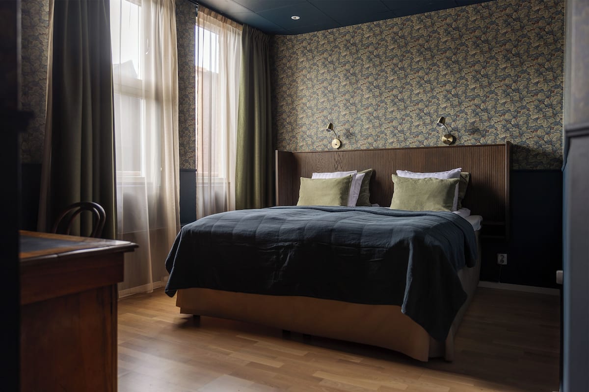 Une chambre à coucher avec un lit en bois, un bureau et une fenêtre avec des rideaux.