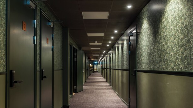 A long, narrow hallway with doors on one side and a patterned wall on the other.