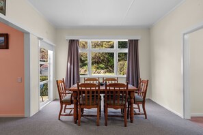 Un espace repas comprenant une table et des chaises, de grandes fenêtres avec des rideaux et un revêtement de sol en moquette.