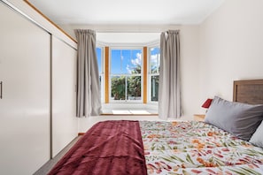 Une chambre à coucher avec un lit, une fenêtre avec des rideaux et une vue sur la verdure à l’extérieur.