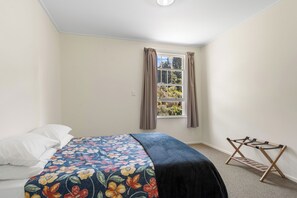 A bedroom with a bed, a window with curtains, and a wooden drying rack.