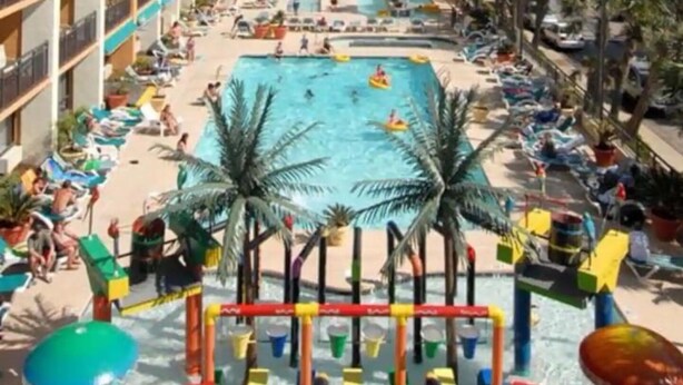 Um hotel com área de piscina, palmeiras e vista para a praia.