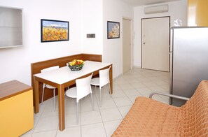 A compact room with a dining table, chairs, a sofa, a refrigerator, and two doors.
