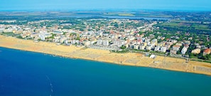 An aerial view of a coastal city with a beach, buildings, and a mix of urban and green areas.