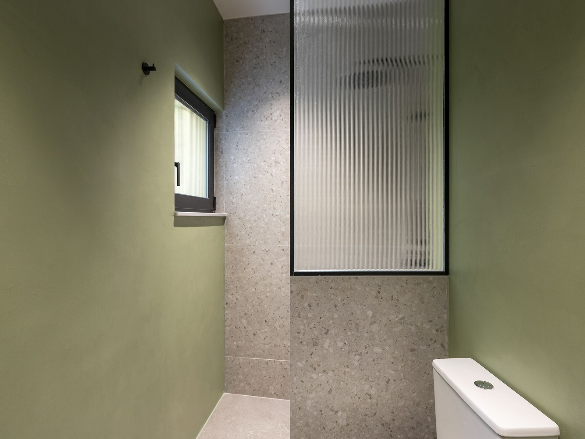 Un couloir étroit avec une fenêtre, un panneau en verre dépoli et des toilettes blanches.