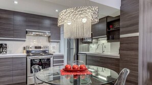 A modern kitchen with dark wood cabinets, stainless steel appliances, and a glass dining table with two chairs. - Les Immeubles Charlevoix - Le Quai St-André 1166 (Québec City)