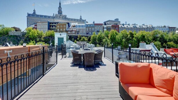 A rooftop terrace with a wooden deck, a table with chairs, and an orange sofa. - Les Immeubles Charlevoix - Le Quai St-André 1166 (Québec City)