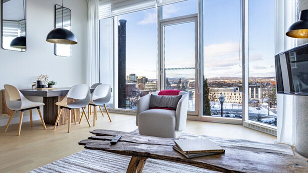 Ein modernes Wohnzimmer mit großem Fenster, einem Essbereich mit Stühlen, einer Couch und einem Holztisch.