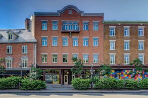 A multi-story brick building with a central entrance, large windows, and a colorful mural on the right side.