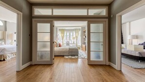 A spacious room with a large bed, a sitting area with a sofa, and a view through a glass door to another room.