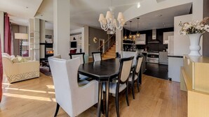 A spacious living area with a dining table, white chairs, and a chandelier.