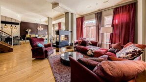 A spacious living room with a fireplace, red curtains, and a modern staircase.