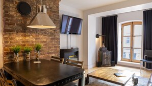 A modern living room with a brick wall, a flat-screen TV, a fireplace, and a large window with curtains.