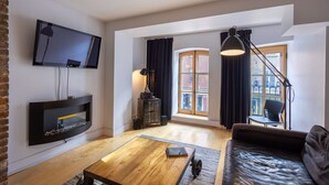 A modern living room with a flat-screen TV, a fireplace, a sofa, a coffee table, and a large window with curtains.