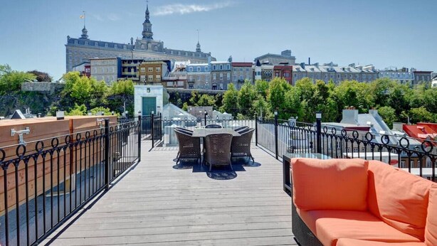 A rooftop terrace with a wooden deck, outdoor seating, and a view of historic buildings in the background.
