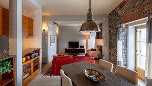 A modern living room with a red sofa, a dining table with a floral bowl, a TV, and a stone wall. - 1002 · Les Immeubles Charlevoix - 1002 (Québec)