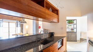 A modern kitchen with granite countertops, a stainless steel sink, wooden cabinets, and a brick backsplash. - 1002 · Les Immeubles Charlevoix - 1002 (Québec)