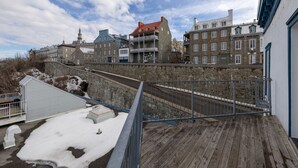 A view of a waterfront property with a wooden deck, stone walls, and traditional buildings with multiple stories and balconies. - 1002 · Les Immeubles Charlevoix - 1002 (Québec)
