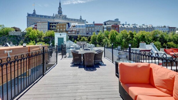 Una terraza en la azotea con mesa y sillas, un sofá y vistas de edificios históricos.