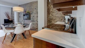 Una cocina moderna con pared de piedra, comedor con sillas blancas y televisor integrado.