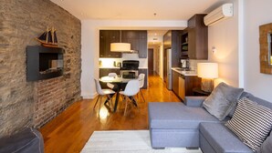 Una sala moderna con un sofá gris, una mesa de comedor con sillas y una cocina con armarios oscuros y horno empotrado.