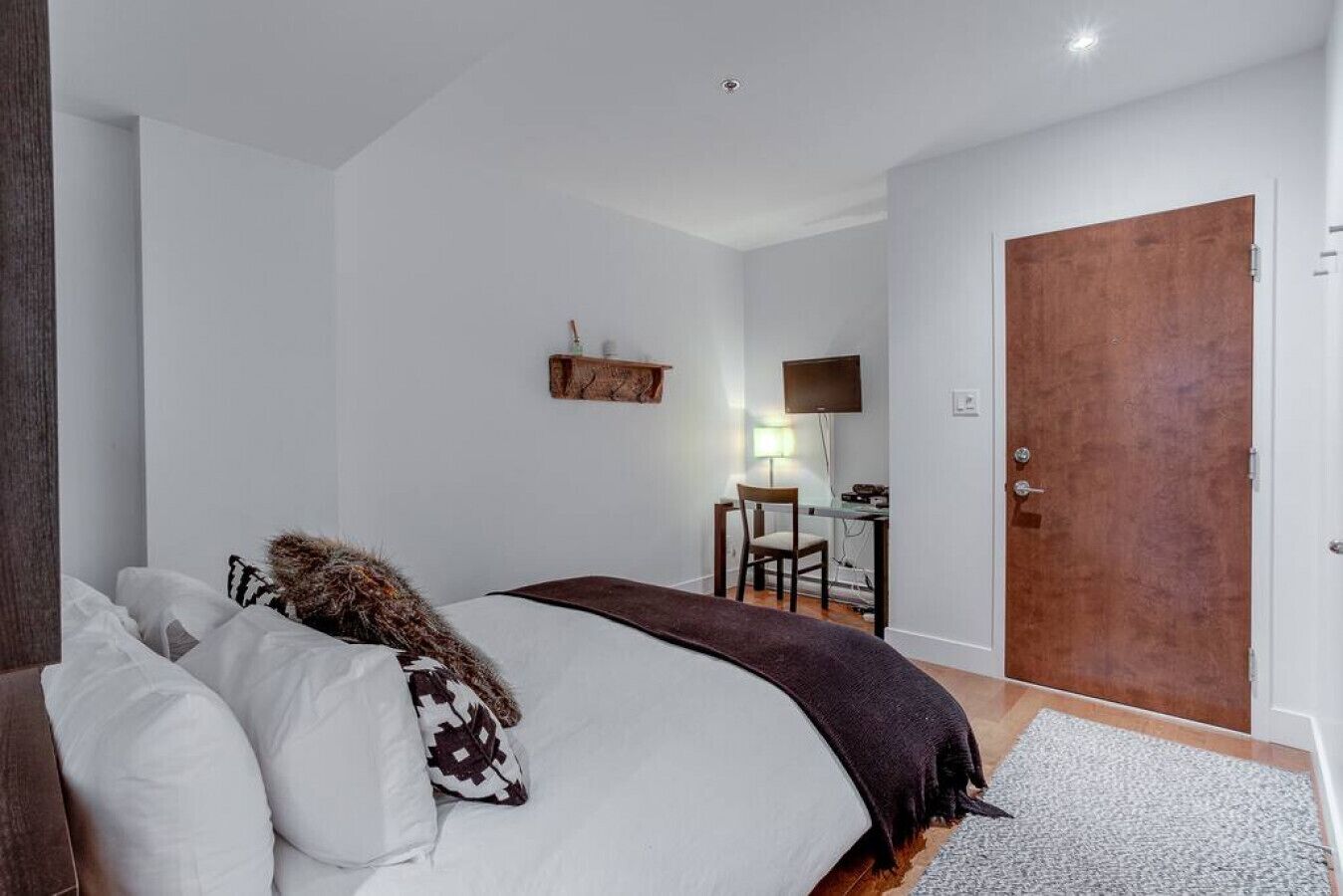 Una camera da letto con un letto grande, una scrivania con una sedia, una televisione e una porta in legno.
