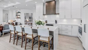 A modern kitchen with white cabinetry, a central island with bar stools, and a dining area with a sofa and chairs.