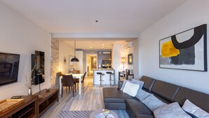 A modern living room with a sofa, coffee table, and TV. There is a kitchen area in the background.