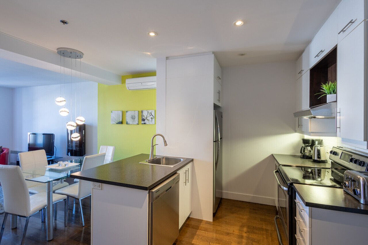 A modern kitchen with a dishwasher, refrigerator, stove, and a small dining area with a glass table and chairs.