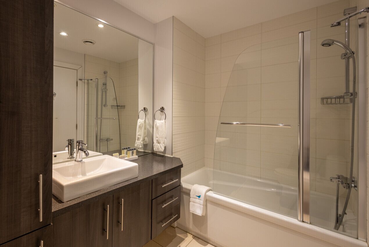 Une salle de bain moderne avec un grand miroir, un lavabo blanc, des meubles en bois foncé, une douche à parois de verre et une baignoire blanche.
