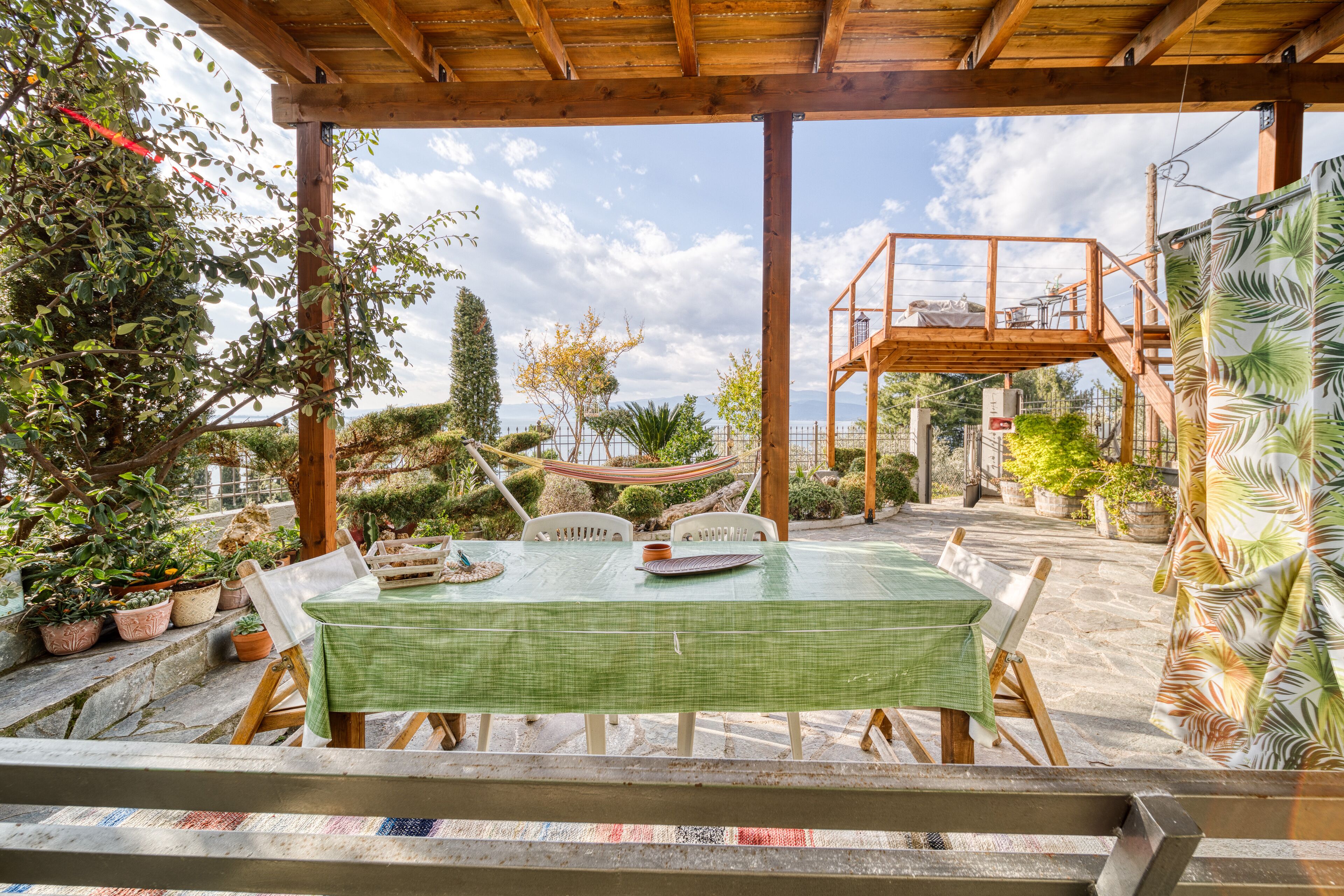 A covered patio with a table and chairs, surrounded by potted plants and a hammock.