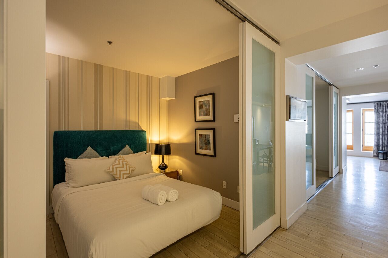 Een hotelkamer met een bed, een nachtkastje, een lamp en een schuifdeur naar een andere ruimte.