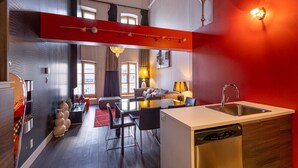 Una cocina moderna con lavavajillas, una zona de comedor con mesa y sillas, un sofá y una pared de acento roja.