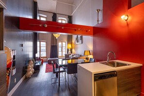 Une cuisine moderne équipée d’un lave-vaisselle, un coin repas avec une table et des chaises, un canapé et un mur d’accent de couleur rouge.
