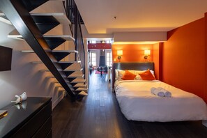 Une chambre d’hôtel comprenant un lit, une table de chevet, un bureau, une chaise, un escalier et donnant sur la salle à manger.