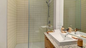 A modern bathroom with a glass-enclosed shower, a large mirror, and a granite countertop with toiletries. - Les Immeubles Charlevoix - 760214 (Ville de Québec)