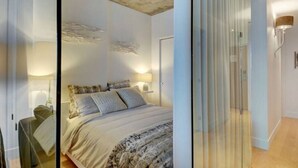 A modern bedroom with a large bed, bedside lamps, and a glass partition. - Les Immeubles Charlevoix - 760214 (Ville de Québec)
