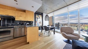 A modern kitchen with stainless steel appliances, wooden cabinets, and a dining area with a view of the city.