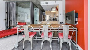 Une cuisine moderne avec un coin repas, comprenant une grande table en bois, des chaises en métal et un mur d’accent de couleur rouge.