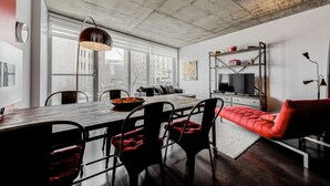 Un salon moderne avec un coin repas, de grandes fenêtres et un plafond en béton.