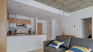 Ein modernes Wohnzimmer mit einem grauen Sofa, bunten Kissen und einer Küchenzeile im Hintergrund.