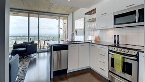 A modern kitchen with a large island, stainless steel appliances, and a view of the city through large windows. - Les Immeubles Charlevoix - 760431 (Ville de Québec)