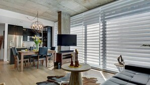 Una sala de estar moderna con un ventanal grande, un televisor de pantalla plana, una zona de comedor y un sofá de cuero.